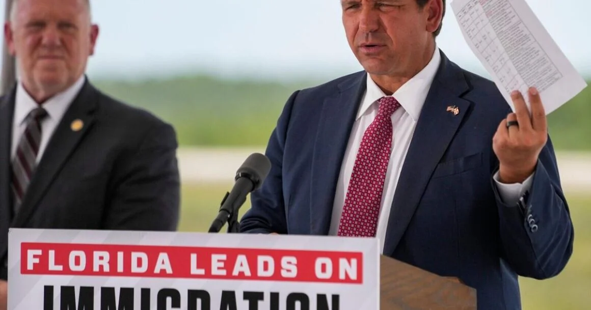 Governor Ron DeSantis holds up a sheet with crimes committed by detainees during a press …