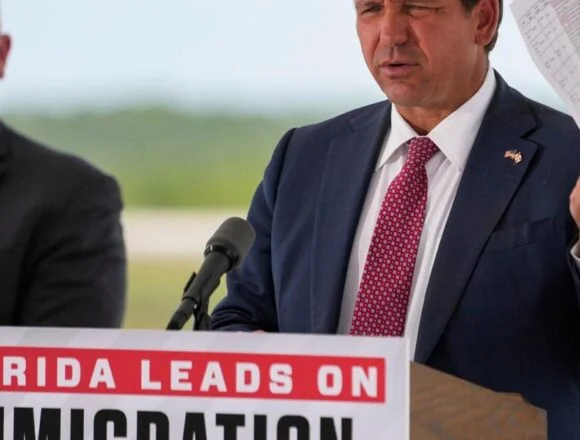 Governor Ron DeSantis holds up a sheet with crimes committed by detainees during a press …